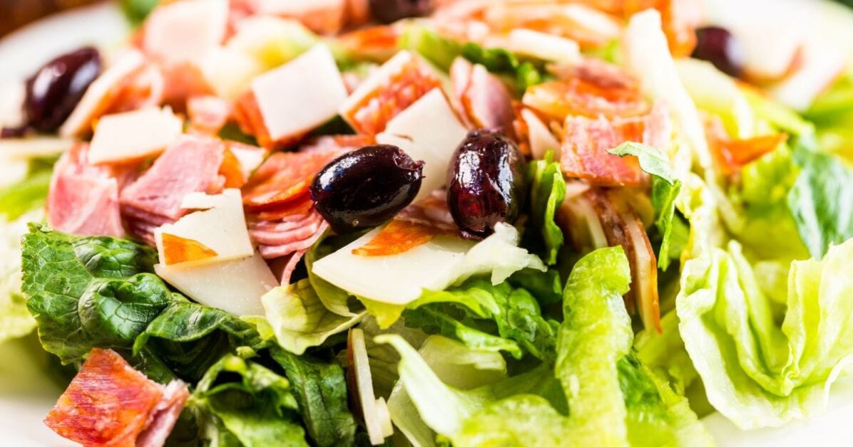 A fresh sub in a tub salad featuring crisp lettuce, sliced salami, pepperoni, cubes of cheese, and black olives.